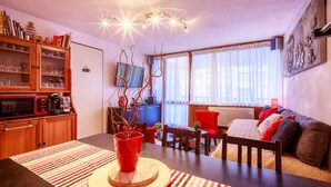 A cozy living room with a dining area, wooden cabinets, a red chair, and a sofa with cushions.