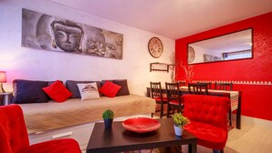 A modern living room with a sofa, red chairs, a dining table, and a Buddha painting.