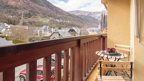 Un balcon avec une balustrade en bois, une petite table avec des chaises, et une vue sur une montagne et la ville en contrebas.