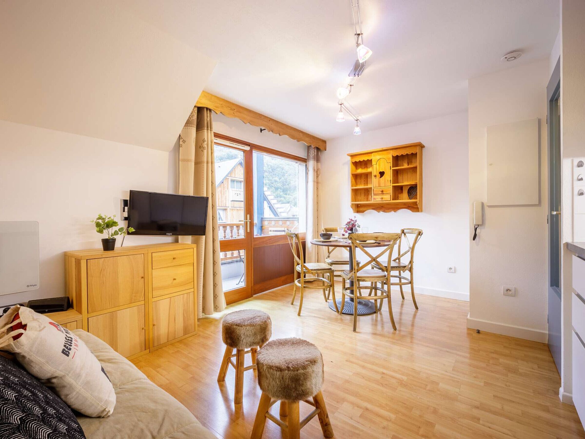 Une pièce chaleureuse avec une table à manger en bois, des chaises, un téléviseur et un petit meuble.