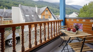 A balcony with a wooden railing, a table with chairs, and a view of buildings and mountains in the background. - Studio cabin for 4 people in Saint Lary Soulan with parking (Saint-Lary-Soulan)