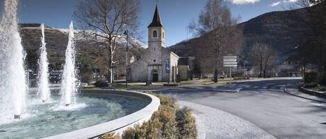 Una iglesia con un campanario, una fuente y un camino adoquinado con acera.