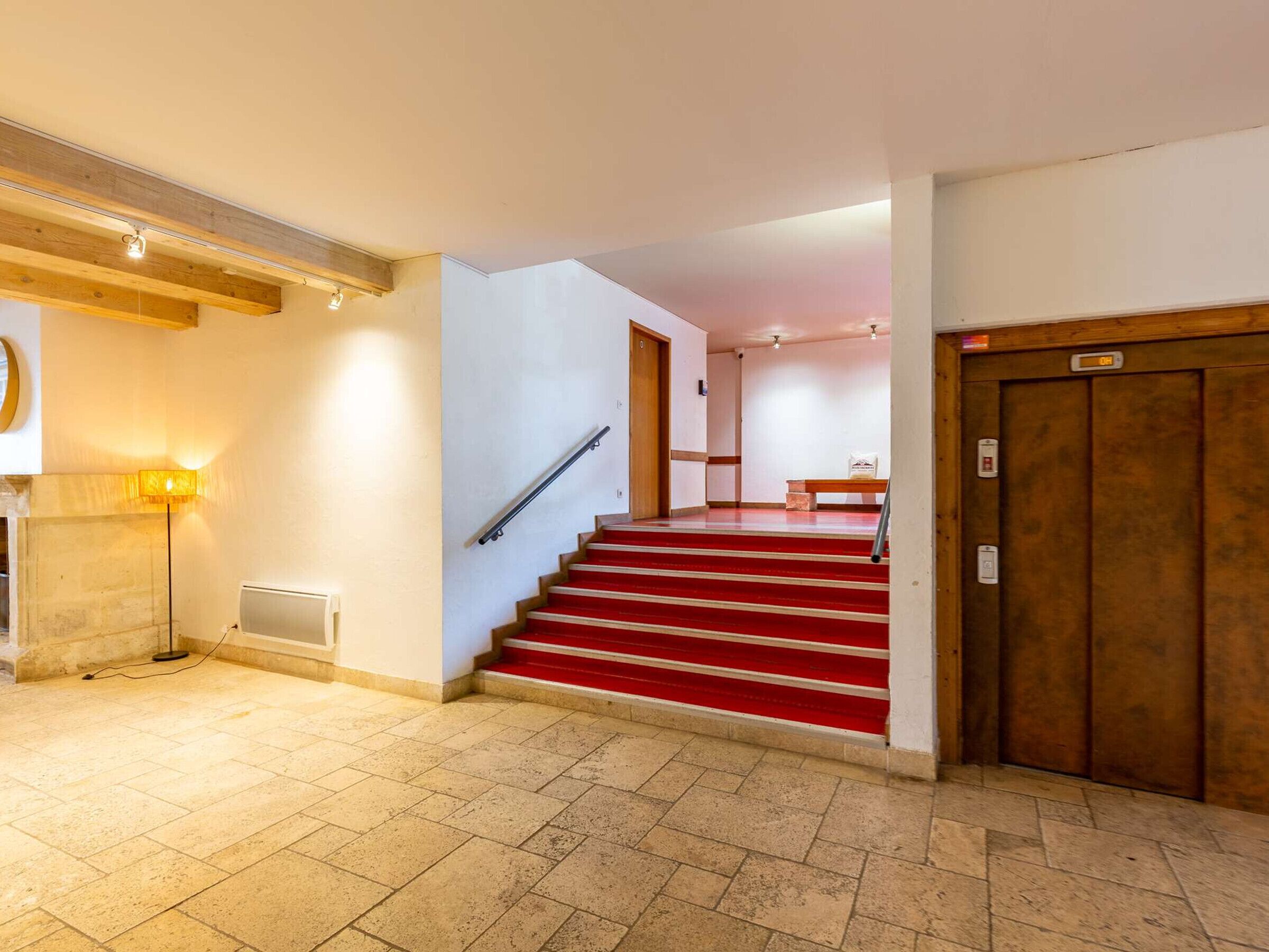 A staircase with red steps leading to a landing, a wooden door, and a wall-mounted light fixture.