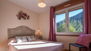 Un dormitorio con cama, mesita de noche, silla, ventana con cortinas y un adorno en la pared.