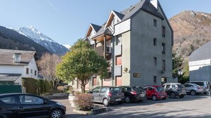 Un edificio de varios pisos con un estacionamiento al frente, rodeado de montañas.