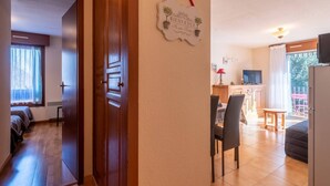 Un salón acogedor con un sofá, una mesa de comedor con sillas, una zona de cocina con un televisor, y un balcón con una silla.