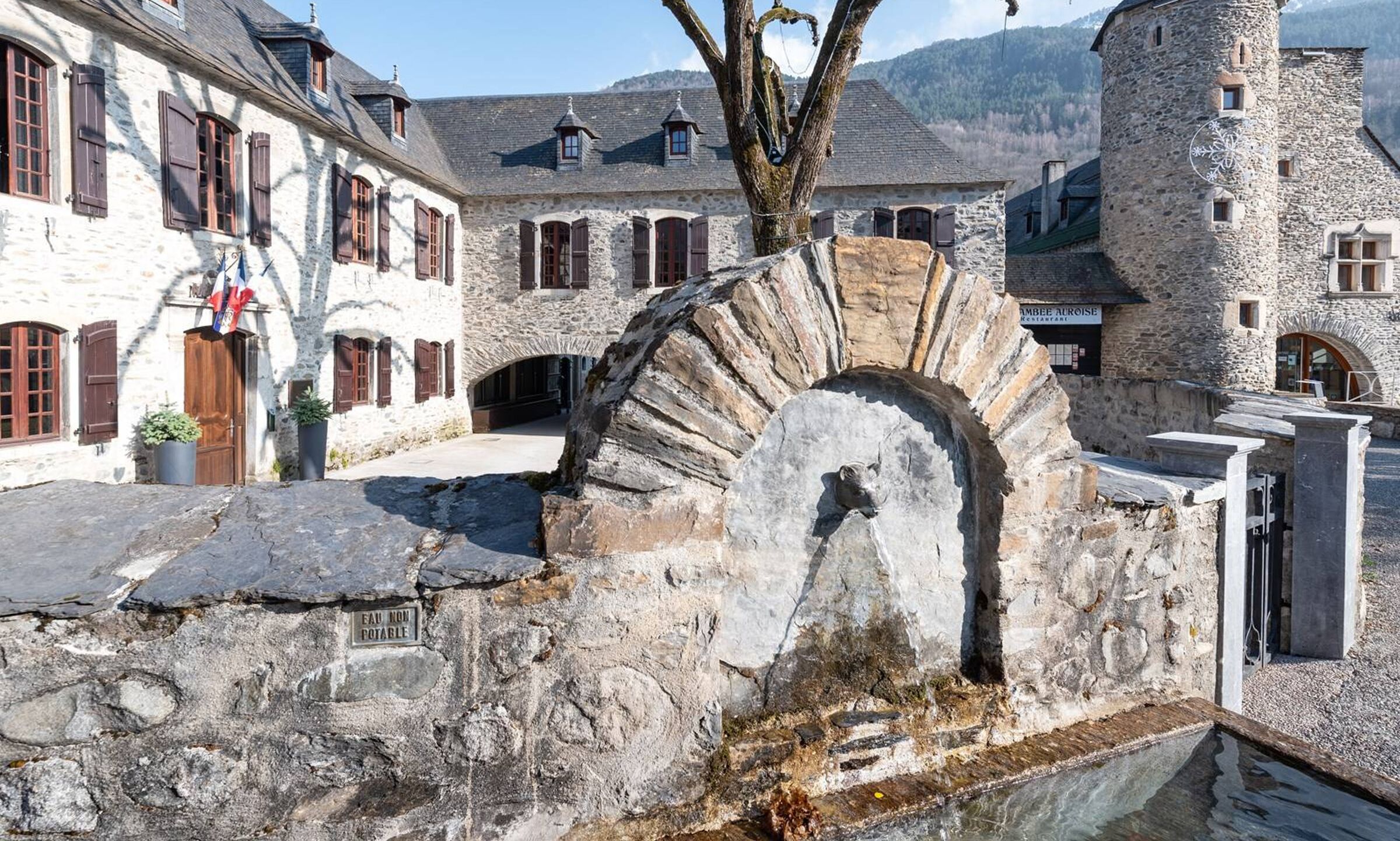A stone building with a large arched entrance, a flag, and a sign indicating 'EAU NON POTABLE' (non-potable water).