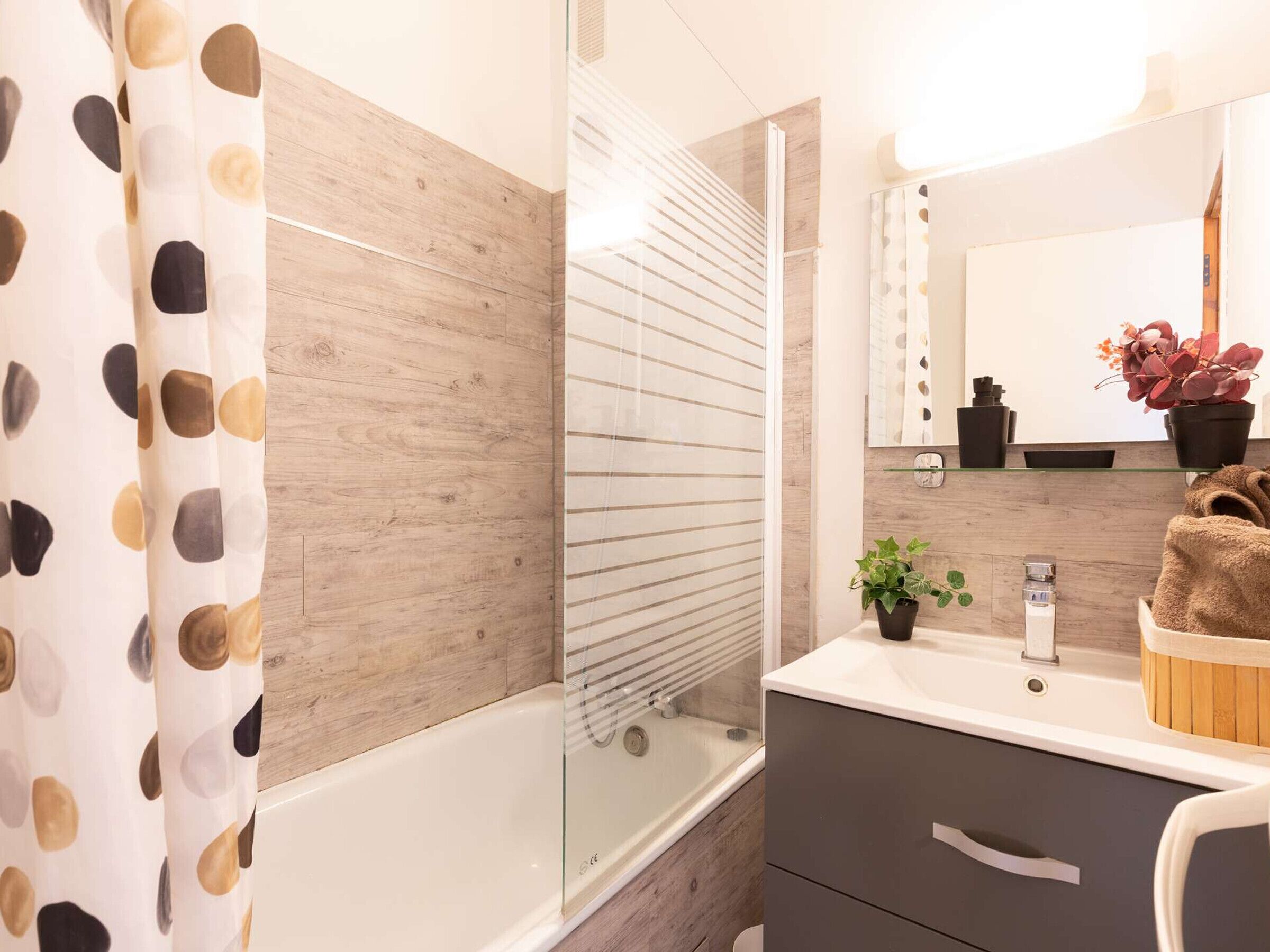 A modern bathroom with a wooden vanity, a glass shower enclosure, and a mirror with a decorative frame.