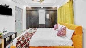 A hotel room with a bed, a television, a desk, and a bathroom with a mirror and curtains. - Butterfly Residency (Chennai)