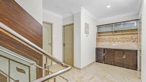 A modern interior with a marble floor, wooden staircase, and a kitchen area with dark cabinets and a tiled backsplash. - Butterfly Residency (Chennai)