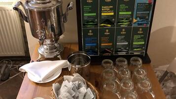 Una mesa de madera con un samovar, bolsitas de té y vasos.