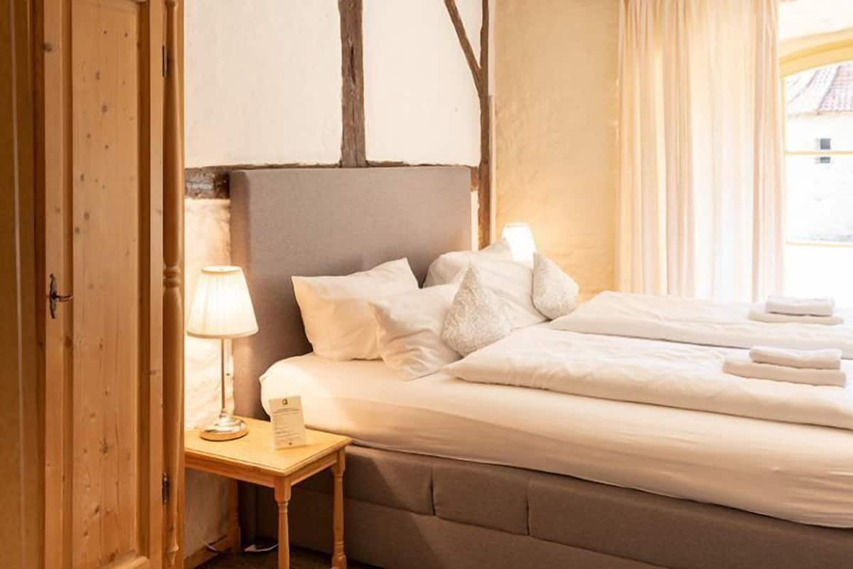 A hotel room with a bed, a nightstand with a lamp, and a window with curtains.