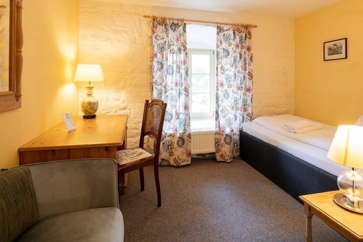 A small, cozy room with a bed, a desk with a lamp, a chair, and a sofa.