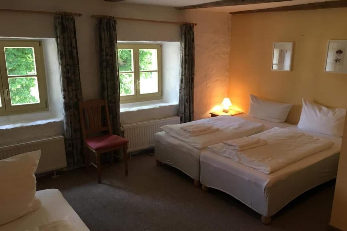 A room with two beds, a chair, a window, and a lamp.