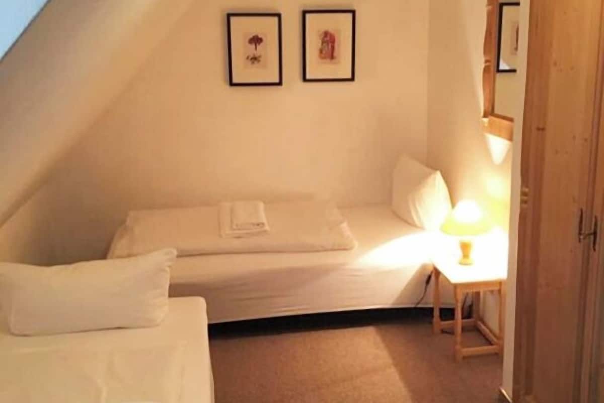 A small, cozy attic bedroom with a single bed, a bedside table with a lamp, and a wardrobe.