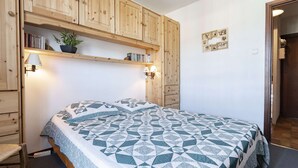 Un dormitorio con cama, armarios de madera, una estantería con libros y una planta, y lámparas fijadas a la pared.