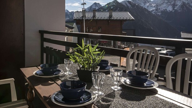 Una mesa lista para comer con vista a la montaña, una planta en maceta y un edificio al fondo.