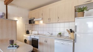 Una cocina moderna con armarios de madera clara, encimera blanca, horno empotrado, lavavajillas y refrigerador.