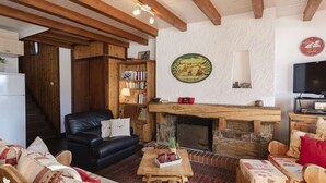Una sala de estar acogedora con chimenea, un sofá de cuero negro, una mesa de centro de madera y una estantería.