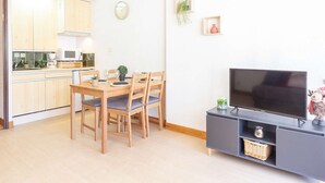 Eine moderne Küche mit Holzschränken, einem Esstisch mit Stühlen, einem Flachbildfernseher auf einem schwarzen Schrank und einer kleinen Pflanze an der Wand.