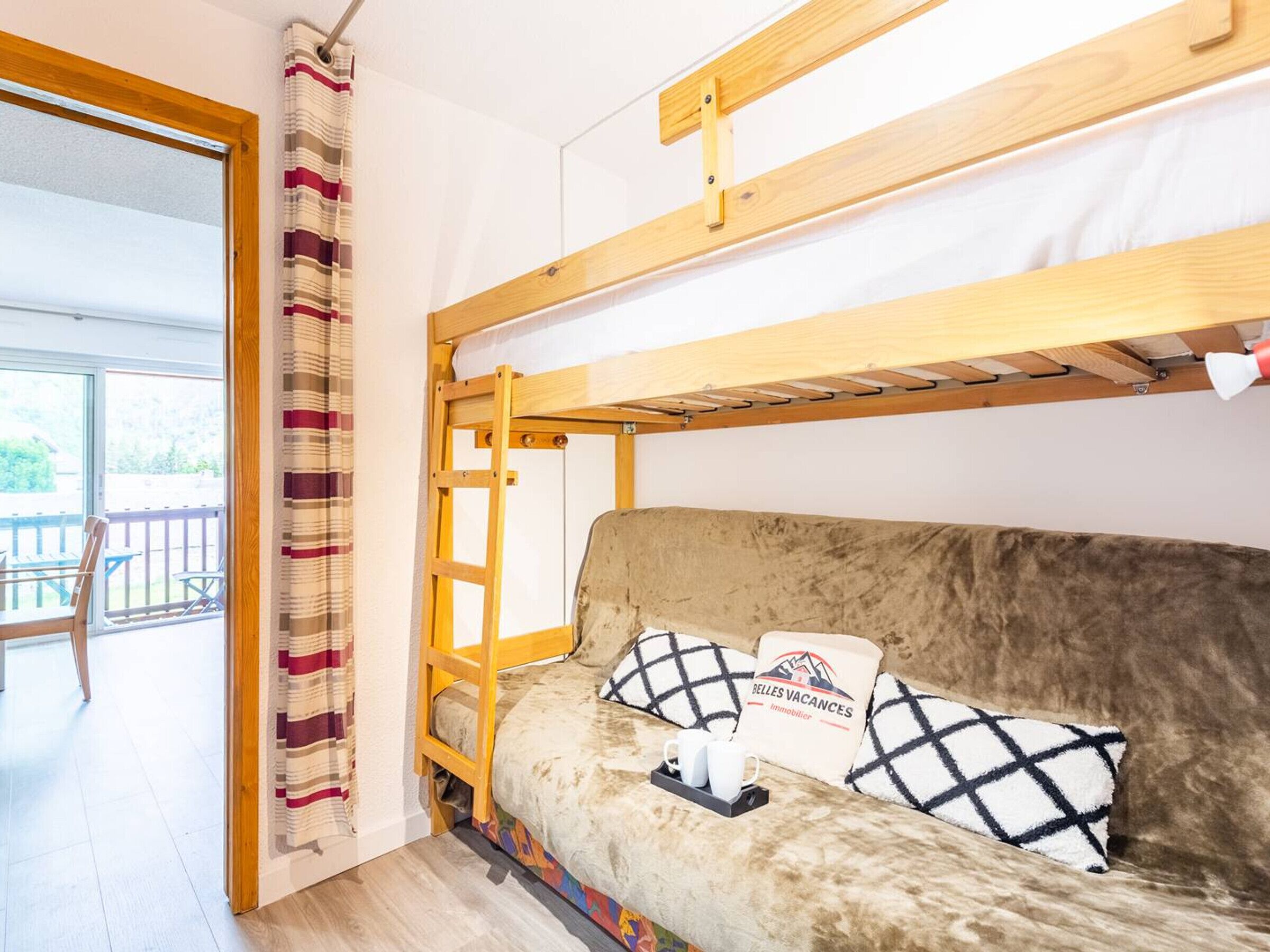 Een stapelbed met een houten frame, een bank met gestreepte kussens, en een bordje op de bank.