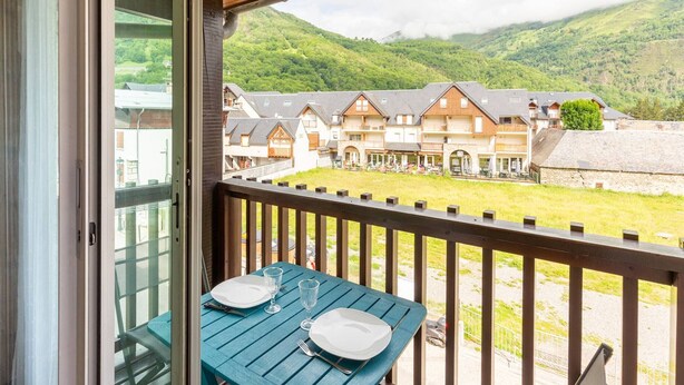 A balcony with a table set for two, overlooking a village with traditional buildings and a mountainous backdrop. - Charming T3 in central Saint Lary Soulan for 11 people (Saint-Lary-Soulan)