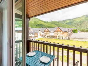 A balcony with a table set for two, overlooking a village with traditional buildings and a mountainous backdrop.