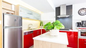 A modern kitchen with a stainless steel refrigerator, red cabinets, a white countertop, a built-in stove, and a clock on the wall. - Charming T3 in central Saint Lary Soulan for 11 people (Saint-Lary-Soulan)