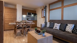 Eine moderne Küche mit Holzausstattung und integriertem Mikrowellenherd. Es gibt einen Essbereich mit einem Holztisch und Stühlen sowie eine Couch mit gemusterten Kissen.