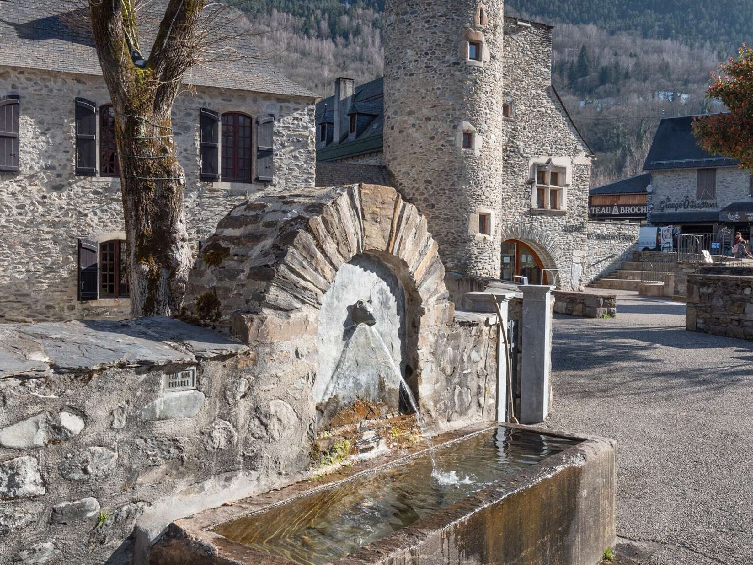A stone building with a tower, a fountain, and a sign that reads "TEAU BROCHE".