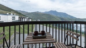 Een balkon met een tafel en twee mokken, met uitzicht op een bergachtig landschap en een wateroppervlak.