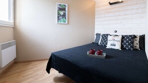 Een slaapkamer met een bed, een raam, een radiator, een wandlamp en een lijst met een afbeelding.