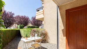 A small outdoor patio area with a table and chairs, a wooden door, and a hedge.