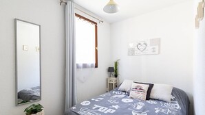 A bedroom with a bed, a bedside table, a lamp, a potted plant, a mirror, and a window with curtains.