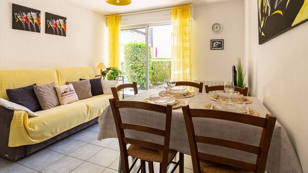 A dining area with a table set for four, a sofa, and a yellow curtain.