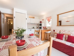 A compact living space with a dining area, kitchenette, and a sofa with red cushions.