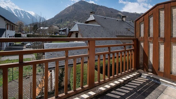 A wooden balcony with a view of a mountain and houses.