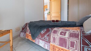 A bedroom with a bed, a wooden chair, a wardrobe, and a door leading to another room.