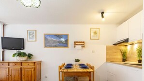 Una cocina compacta con una mesa de comedor preparada para cuatro personas, armarios de madera, un televisor montado en la pared y cuadros enmarcados.