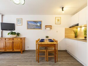 Una cocina compacta con una mesa de comedor preparada para cuatro personas, armarios de madera, un televisor montado en la pared y cuadros enmarcados.
