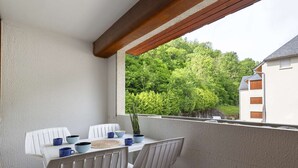 Un balcón con una mesa y sillas, una planta en maceta y vistas a una zona boscosa.