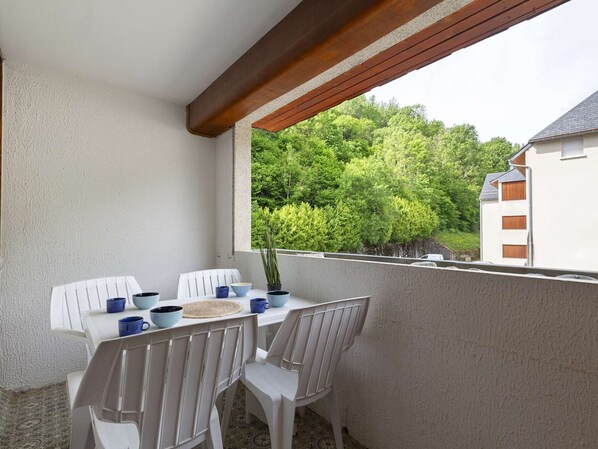A balcony with a table and chairs, a potted plant, and a view of a forested area.