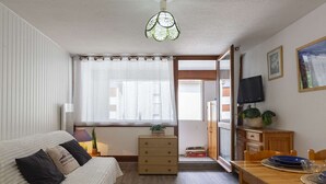 Una habitación acogedora con una cama, una pequeña mesa de madera, un televisor y un ventanal con cortinas.