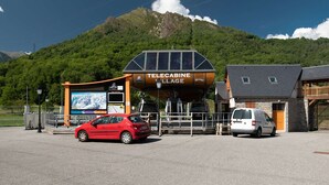 Un pueblo con telecabina que presenta una estructura de madera, un coche rojo y una furgoneta blanca estacionados al frente.