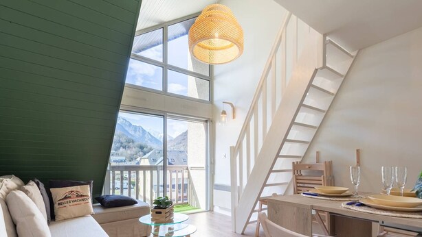A modern interior with a sofa, a small round table, a wooden chair, and a dining area with a table set for two.