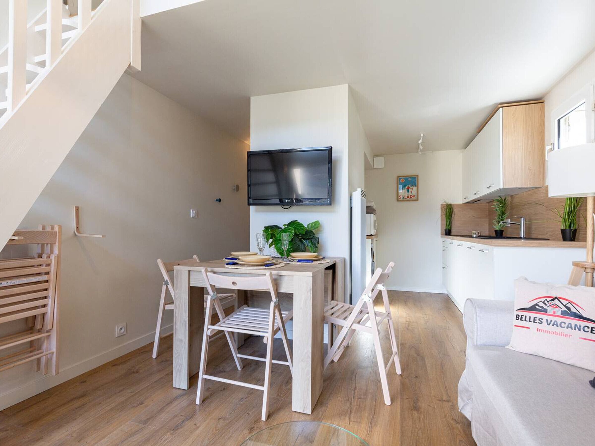 Une cuisine moderne dotée d’un téléviseur à écran plat, de meubles en bois et d’un coin repas avec une table et des chaises.