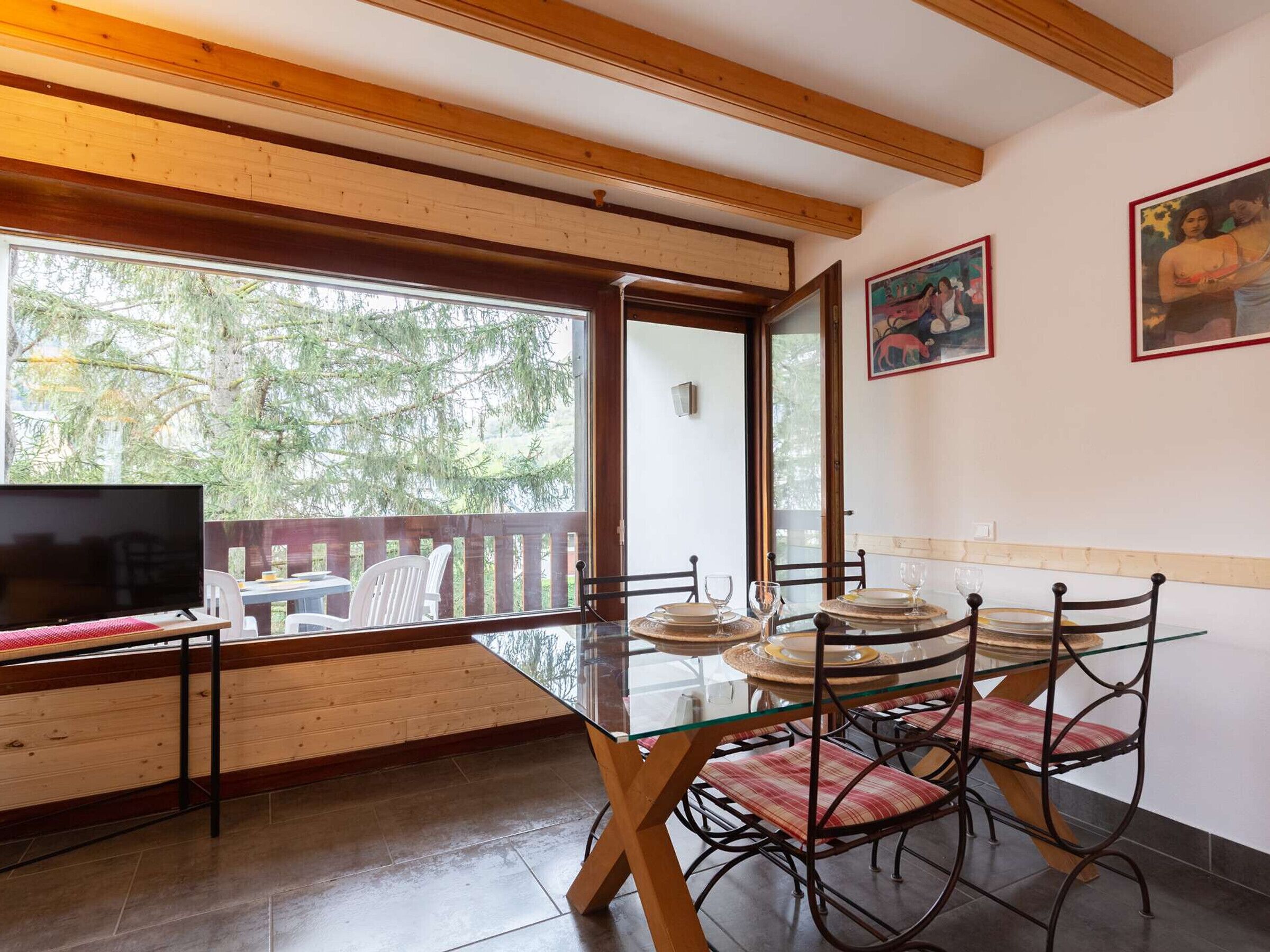 A dining area with a glass table, metal chairs, and a TV on a wooden table.