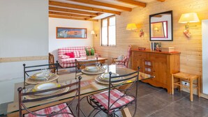 Un comedor acogedor con una mesa de madera dispuesta para cuatro personas, rodeada de sillas con cojines de cuadros. También se puede ver un banco de madera y un taburete pequeño.