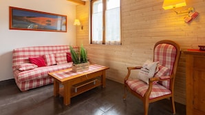Una habitación acogedora con un sofá a cuadros, una silla de madera, una mesita y una ventana con vistas.