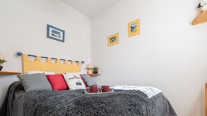 Une chambre à coucher avec un lit, des oreillers, une couverture, deux tables de chevet avec des lampes et des tableaux encadrés accrochés au mur.